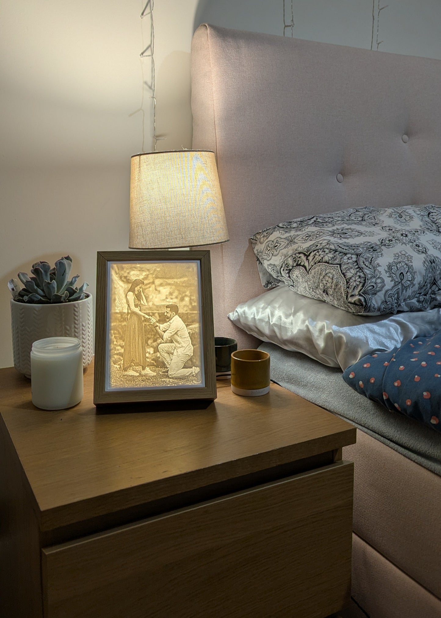Nighstand with lamp, framed artwork, and decorative items in a bedroom setting.